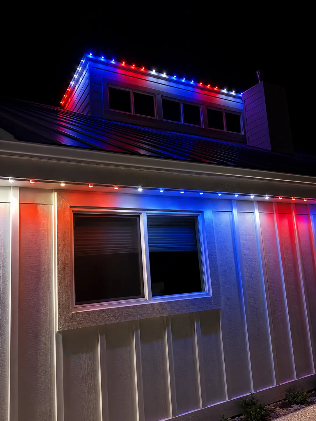 Red, white, and blue permanent roofline lighting on a home at night